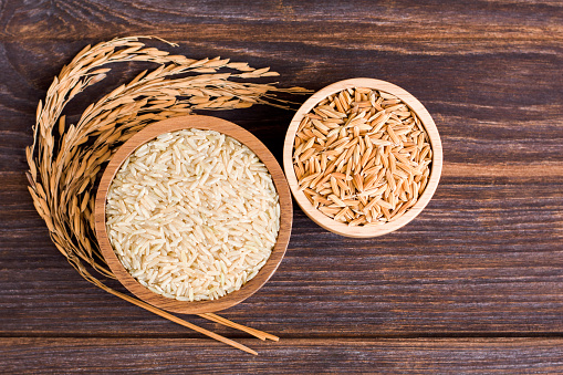 Brown rice, natural long rice grains (Thai jasmine rice) and paddy rice in wooden bowl isolated on wooden table background. Top view. flat lay.