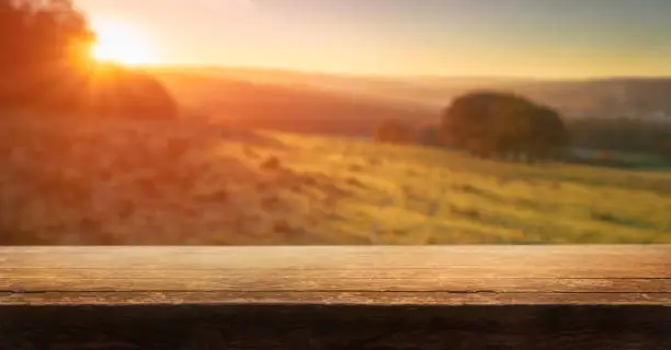 Photo of A wooden table top product display with a blurred background scene of golden sunset fields.