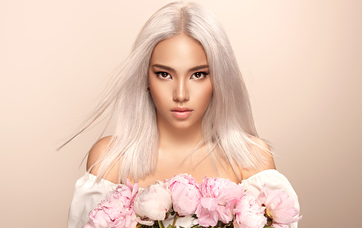 Portrait of black eyed beautiful woman with asian appearance and  wearing in exquisite makeup.Elegant long hair dyed in the shades of blonde.Model straightly gazing at the viewer. Hairstyling, dye of hair, cosmetics and makeup.