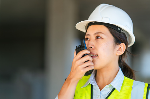 A young female engineer is using a walkie-talkie on a construction site.