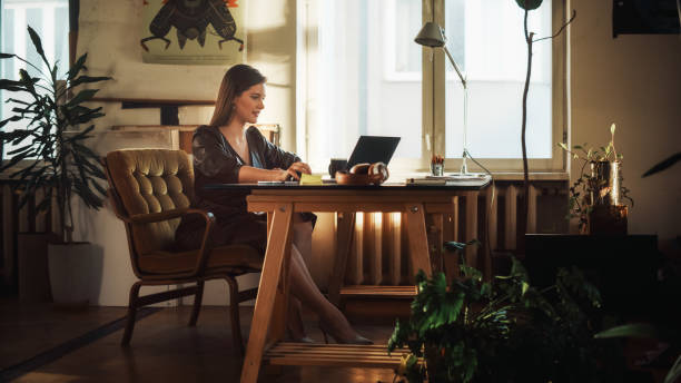 istock Young Beautiful Female Works on a Laptop Computer in Creative Agency in Authentic Loft Office. Renovated Stylish Design with House Plants, Artistic Posters and Big Windows. 1338090442