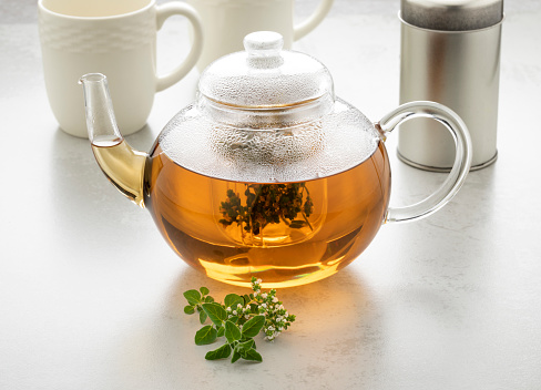 Glass teapot with oregano tea and a fresh twig of oregano in front