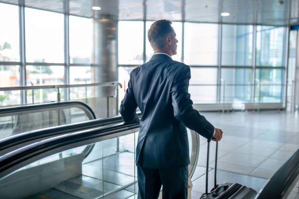 istock Back view of man with suitcase on escalator 1338092576