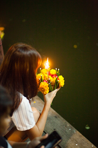 Young thai woman is praying at Loi Krathong at canal in Bangkok Ladprao. Woman has flower bouquet with candle in hands. One of most important buddhist days in Thailand