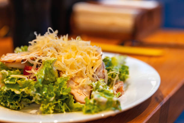 Meat salad with greens and tomatoes covered with grated cheese on a white plate