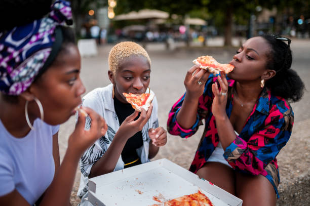 three friends are sitting outside eating pizza - pizza eating african descent lunch imagens e fotografias de stock