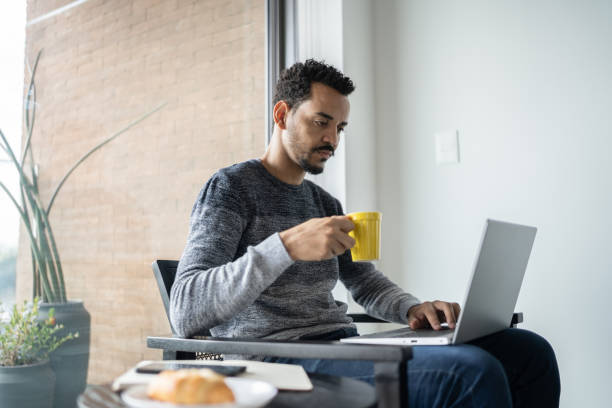 istock Man holding a mug and typing on the laptop at home 1338097255