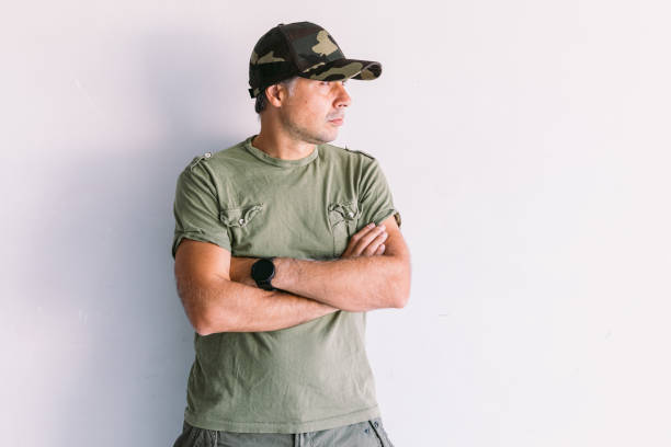 istock Military man with camouflage cap, arms crossed, on a white wall 1338098800