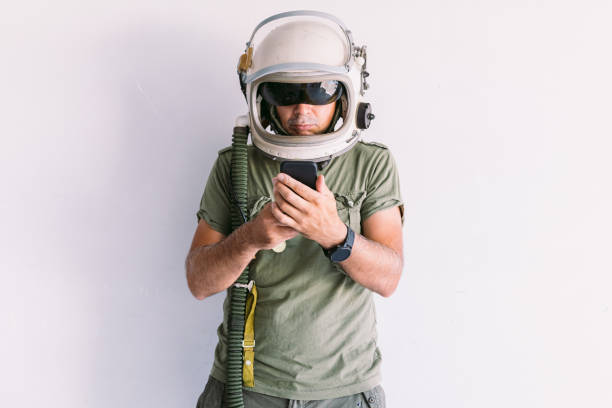 Military man with astronaut cosmonaut helmet, looking at mobile phone, on a white wall stock photo