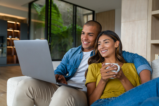 Happy Latin American couple relaxing at home watching movies on their laptop and smiling - lifestyle concepts