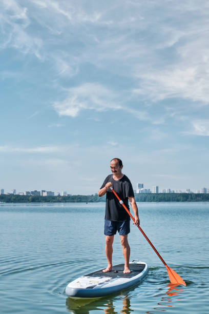 istock Asian older man on sup board on calm lake. 1338100138