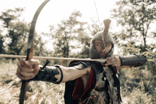 istock Ancient warrior archer aims and shoots from bow among meadow. 1338101291