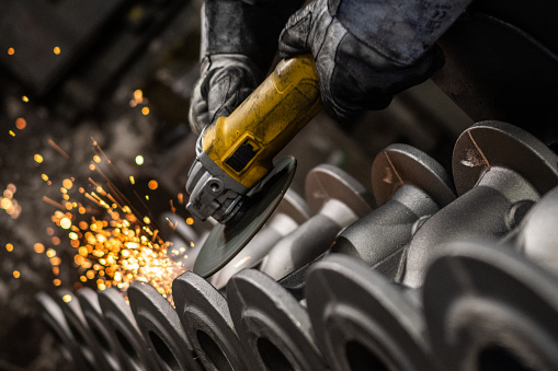 Close-up of metal worker's hands grinding metal equipment with grinder in steel mill.