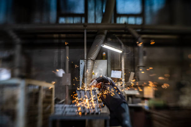 Mature man grinding metal manufactured from recycled metal with grinder in steel mill.