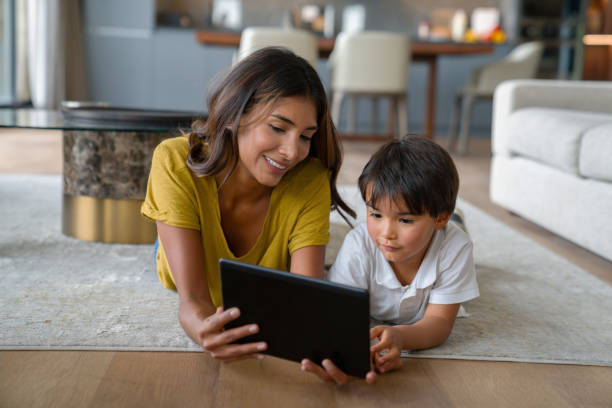 Happy mother and son at home watching a movie together on a tablet Happy mother and son relaxing together at home watching a movie on a tablet while lying down on the floor - lifestyle concepts woman lying on the floor isolated stock pictures, royalty-free photos & images