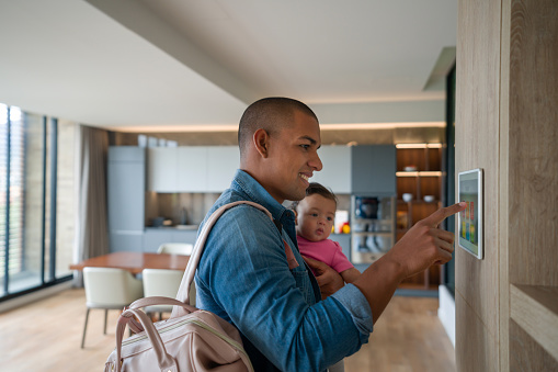 Happy Latin American man leaving the house with his baby and locking the door using a home automation system â smart home concepts