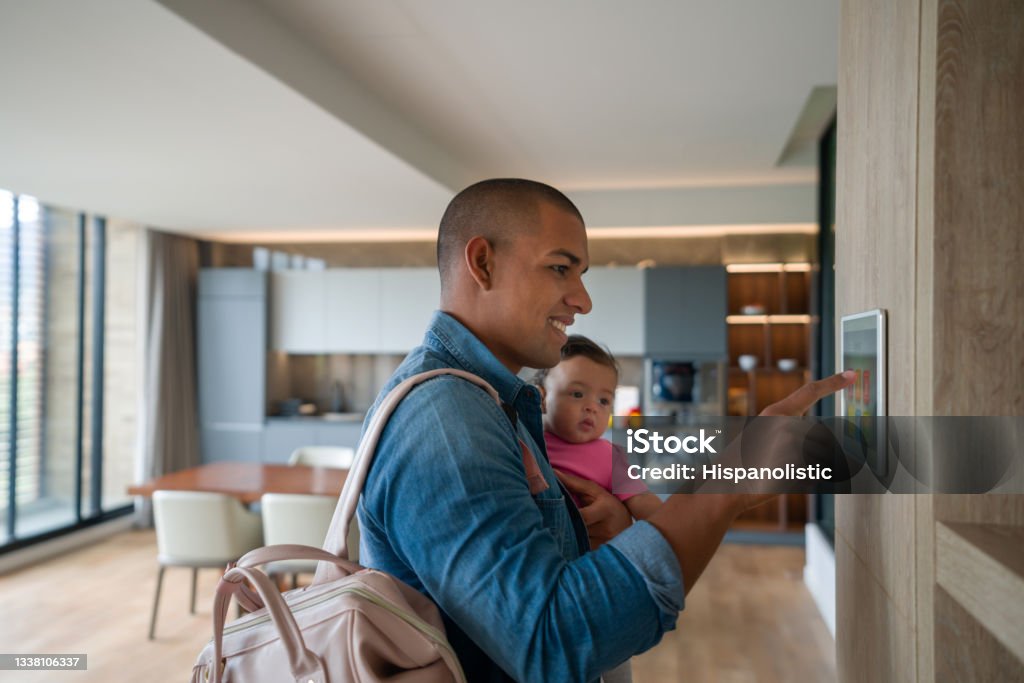 Man leaving the house with his baby and locking the door using a home automation system Happy Latin American man leaving the house with his baby and locking the door using a home automation system â smart home concepts Home Automation Stock Photo
