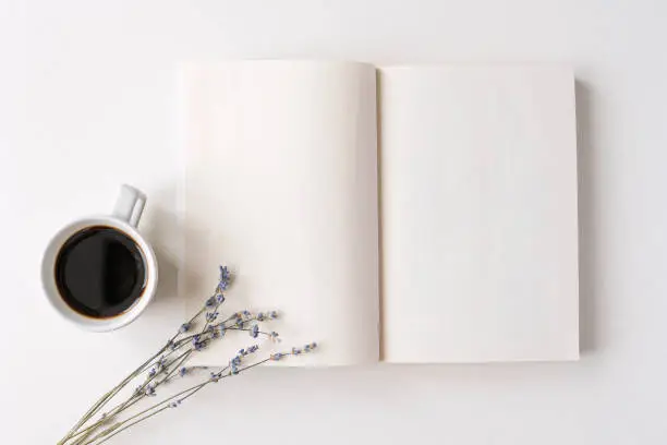 Photo of Opened notepad, book with white blank sheets on a desk. Hot black coffee, dry lavender bouquet. Morning mood, space for text