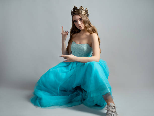 fajna księżniczka w bujnej niebieskiej sukience i koronie wykonuje gest dłoni rockera, - women crown princess 20s zdjęcia i obrazy z banku zdjęć