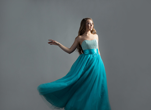 wonderful dancing princess in a lush blue dress, a young beautiful blonde with long curls, spinning on a gray background