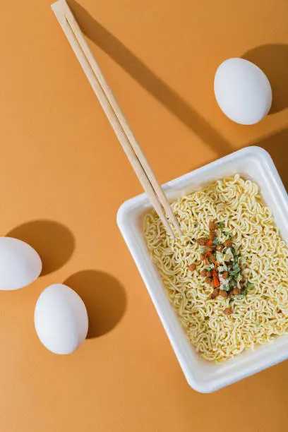 Instant noodles with egg and meat, in a plastic plate. Fast, nourishing lunch and dinner every day. Orange background, top view