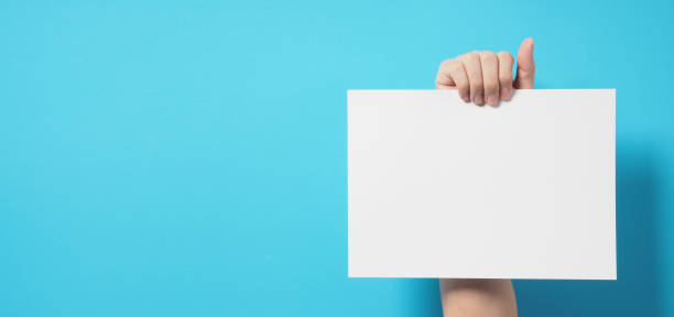 istock One hand is holding the white A4 paper on blue background. 1338110002