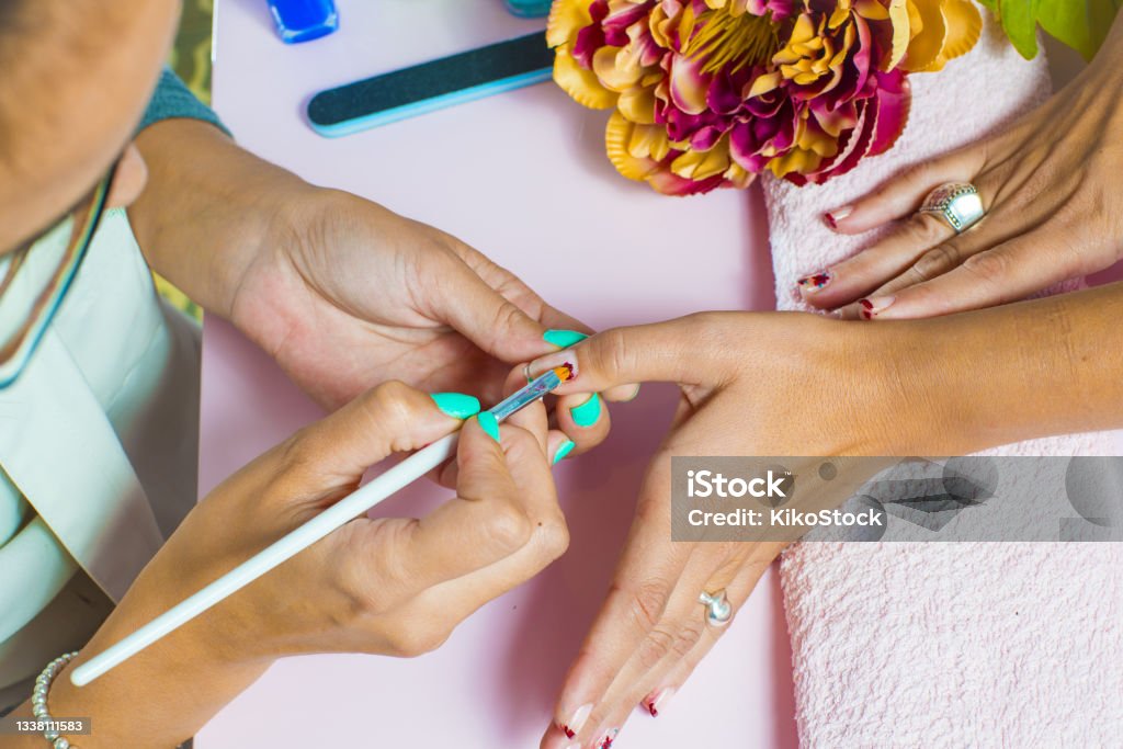 Woman getting a manicure and nail painting in the foreground Acrylic Painting Stock Photo
