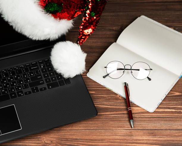 istock Christmas composition, santa hat, laptop, glasses, note book, on a wooden background. 1338114845