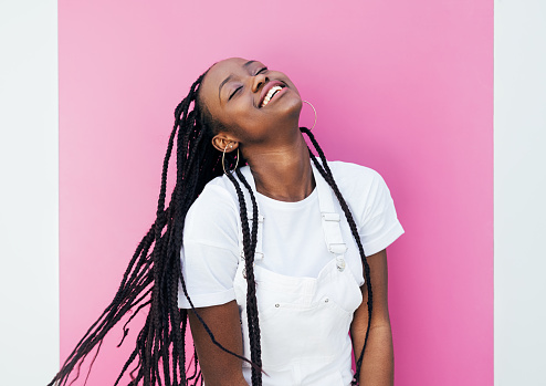 Happy woman with braids standing at pink wall outdoors with closed eyes