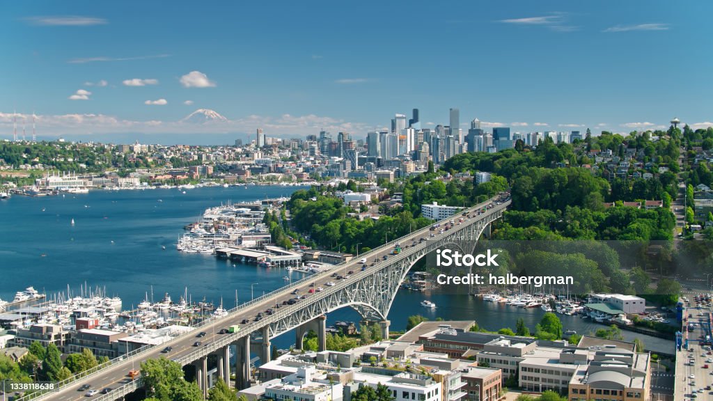 Drone Shot of Seattle with Mt Rainier in Distance Aerial shot of Seattle, Washington on a sunny day in summer, looking along the Aurora Bridge from the Fremont bank of Lake Union towards East Queen Anne and Eastlake, with the downtown skyline in the distance and, much further away, the snowcap of Mount Rainier. Seattle Stock Photo