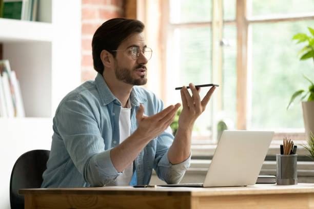 man sit indoors holds cellphone talks to client on speakerphone - conference phone imagens e fotografias de stock