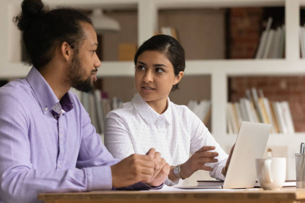 istock Two multiethnic colleagues sit at desk communicating discuss current business 1338121100