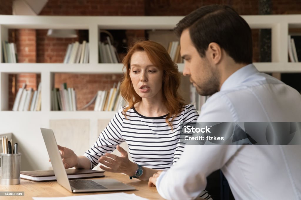 Sales manager showing to client online presentation on laptop Discussion of new corporate app, business negotiations, sales manager showing to client online presentation concept. Young woman talk to colleagues sit at desk working together look at laptop screen Feedback Stock Photo