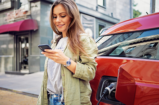 Portrait of young woman charging her electric car