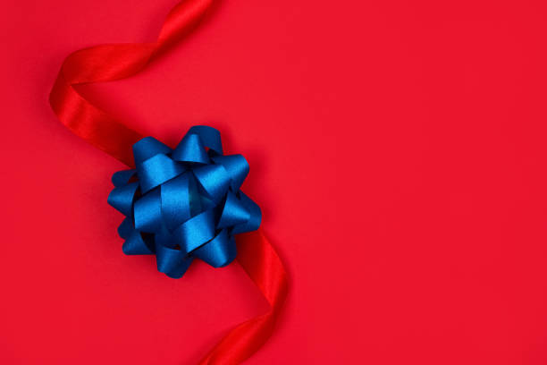 istock Festive background with decorative blue ribbon bow on red background with copy space for text. Festive composition for greeting card design, giving presents, holidays sale or giveaway concept 1338134455