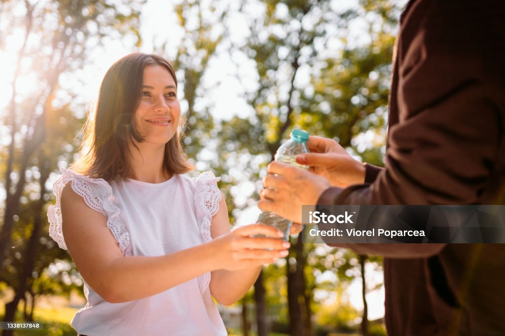 Smart pretty young woman in white blouse giving a bottle of water to a homeless poor man in old brown jacket, volunteer mission concept. Smart pretty young woman in white blouse giving a bottle of water to a homeless poor man in old brown jacket, volunteer mission concept. High quality photo Begging - Social Issue Stock Photo