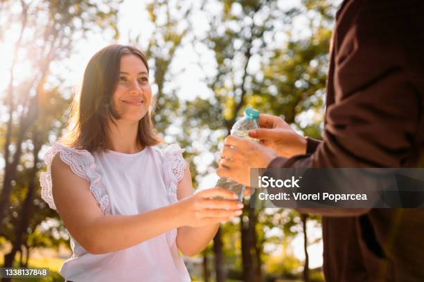 Smart Pretty Young Woman In White Blouse Giving A Bottle Of Water To A Homeless Poor Man In Old Brown Jacket Volunteer Mission Concept Stock Photo - Download Image Now
