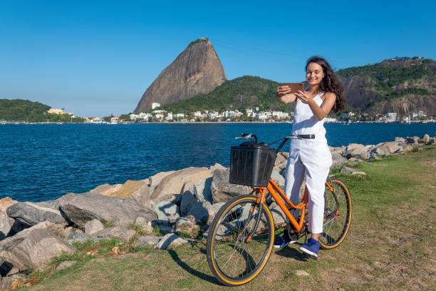 una joven se toma una selfie en el parque flamengo con la montaña pan de azúcar al fondo. - brazil bicycle rio de janeiro outdoors fotografías e imágenes de stock