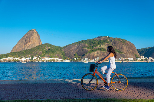 24 year old caucasian woman rides on the bike path in front of the Sugarloaf in Flamengo Park, at the border of Guanabara Bay