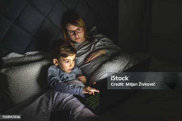 Mother And Son Watching Movie Or Cartoon Using Laptop In Bed At Nighttime Small Boy And His Mom Using Computer While Lying In Bed At Night In Dark Room Leisure Activity Family Bedtime Concept Stock Photo - Download Image Now