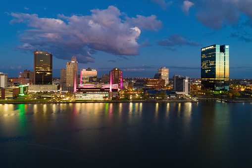 Downtown Toledo skyline aerial at dusk with sunset reflections on buildings and the Maumee River in the foreground and cumulus clouds in the background.