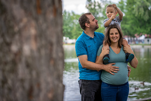 A father and a pregnant mother trying to take a family portrait with their young boy in public park Pie-XII of Trois-Rivières city, Quebec, during summer.