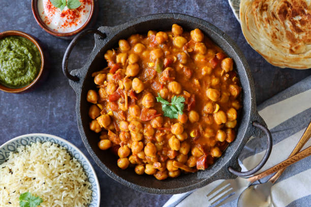 zbliżenie przedstawiające miskę kadhai serwującą domowej roboty pendżabskie chole (curry z ciecierzycy), lachha paratha (płaski chleb), miskę białego ryżu, raita (sos na bazie jogurtu), dipy chutney z kolendry miętowej, sztućce, ręcznik herbac - cieciorki zdjęcia i obrazy z banku zdjęć