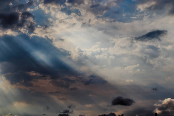 small black tufts of cloud floating under a dramatic blue sky, with clouds illuminated by sunbeams - POA, SAO PAULO, BRAZIL.