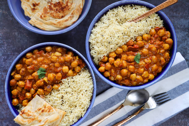 bild blaue teller hausgemachte punjabi chole (kichererbsencurry) mahlzeit, weißer reis, lachha paratha (fladenbrot), löffel, gabel, gestreiftes geschirrtuch, melierter blauer hintergrund, erhöhte ansicht - currypulver stock-fotos und bilder