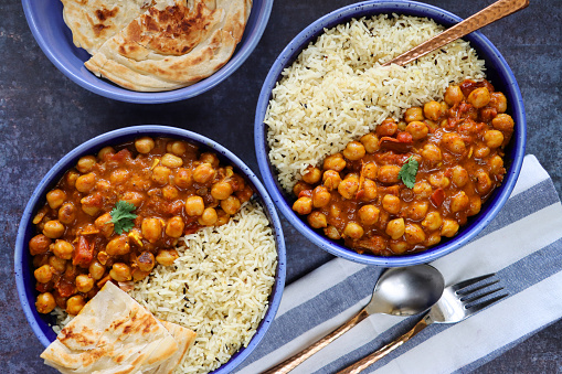 Stock photo showing elevated view of homemade Punjabi chole (chickpea curry) meal on blue plates with white rice. Soaked chickpeas flavoured with bay leaves, cardamom, cinnamon stick and salt, cooked with grated onion, cloves, ginger-garlic paste, tomato puree, chole masala, red chilli, paprika and cumin powder, sliced ginger and garnished with coriander.