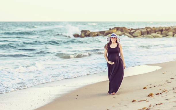 istock Pregnant woman smiles while walking along an idyllic beach 1338176982