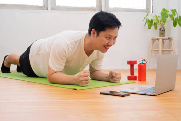 istock Training At Home. Sporty man doing yoga plank while watching online tutorial on laptop 1338183704