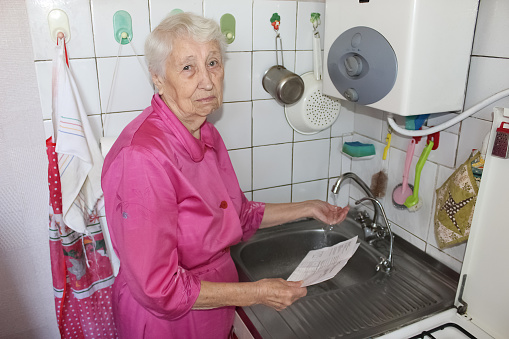 Terrified senior poor woman is checking water meter at home- consumption and expensive water concept