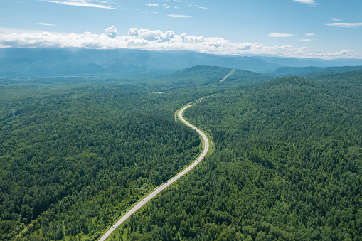 Aerial view of the road of Lake Baikal. A road passing through a coniferous forest, aerial photography from a drone. Winding road in the West Siberian taiga ecoregion
